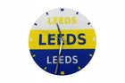 A circular wall clock featuring the Leeds club colors, with a white top half, yellow middle band, and blue bottom half, all printed with the word 'LEEDS'. The clock has silver hands and small blue and white hour markers.