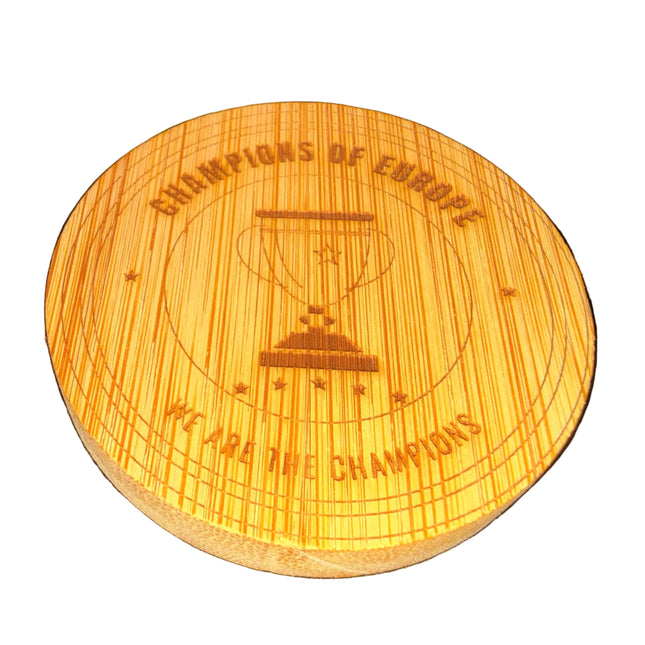 A round wooden coasters featuring a laser-engraved design of an hourglass, a soccer ball, and the text 'CHAMPIONS OF EUROPE' and 'WE ARE THE CHAMPIONS' on a dark textured background.