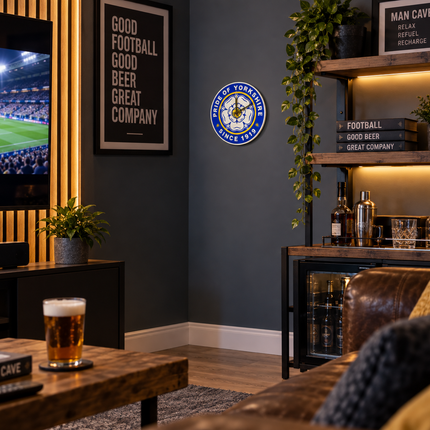 A framed circular 'Sporting York' wall clock is displayed on a dark gray wall in a modern, dimly lit man cave living room setup with a TV, wooden shelves, and a bar cabinet.