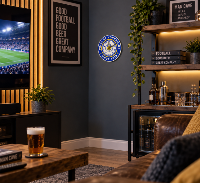 A framed circular 'Sporting York' wall clock is displayed on a dark gray wall in a modern, dimly lit man cave living room setup with a TV, wooden shelves, and a bar cabinet.
