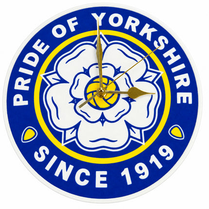 A round wall clock featuring the blue, white, and yellow crest of Pride of Yorkshire, with white hands and no traditional hour markers.