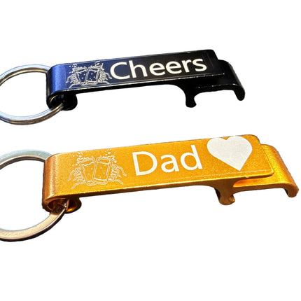 Two bottle opener keychains. The top keychain is black with silver metal rings and the word 'Cheers' in white.